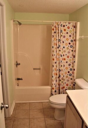 A bathroom with a bathtub, toilet, and a shower curtain with a polka dot pattern. - Oceanfront spacious Condo w/ Stunning Views & Pool Access By Williamson Realty (Ocean Isle Beach)