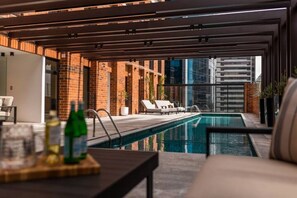Zona de piscina interior moderna con vistas despejadas al horizonte de la ciudad, una pared de ladrillo y sillones de descanso.