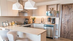 Een moderne keuken met een centraal eiland, barkrukken, een vaatwasser en een koffieapparaat.