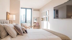 Een moderne hotelkamer met een groot bed, een aan de muur bevestigde televisie en uitzicht op de stad door het raam.