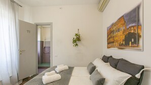 Habitación de hotel con cama, ducha, toallero y un cuadro del Coliseo.