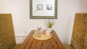 Una mesa de madera con dos sillas tejidas, un cuadro en la pared y una pequeña planta en maceta.
