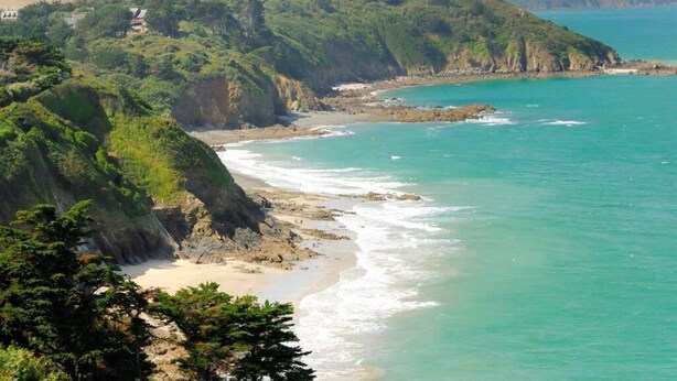 A coastal landscape with a beach, cliffs, and a clear view of the ocean.