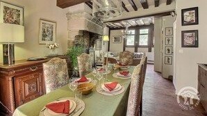 A dining room with a long table set for six, wooden chairs, a chandelier, and framed artwork on the walls.