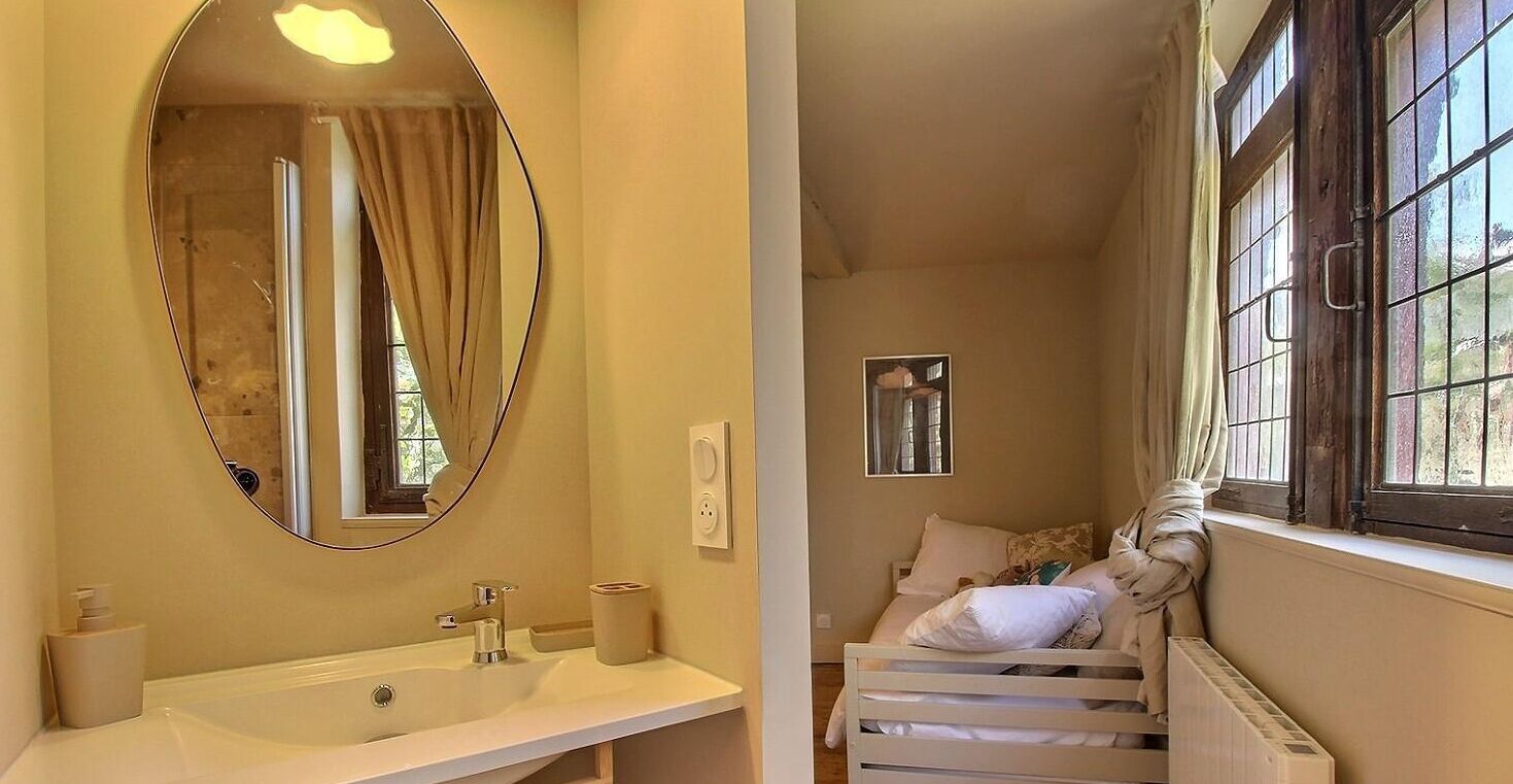 A bathroom with a large oval mirror, a sink, and a window with curtains.