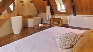 A bedroom with a large bed, a vanity with a sink, a bathtub, and a chair.