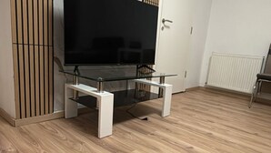 Ein Zimmer mit einem TV-Stand aus Glas, Holzboden, einem weißen Heizkörper und einer Tür.