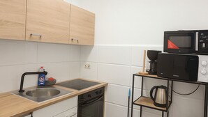 Eine Küche mit Holzschränken, einer Edelstahlspüle, einer Mikrowelle und einem Wasserkocher auf einem Regal.