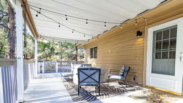 Une terrasse couverte, décorée de guirlandes lumineuses, avec une porte en bois et du mobilier d’extérieur.