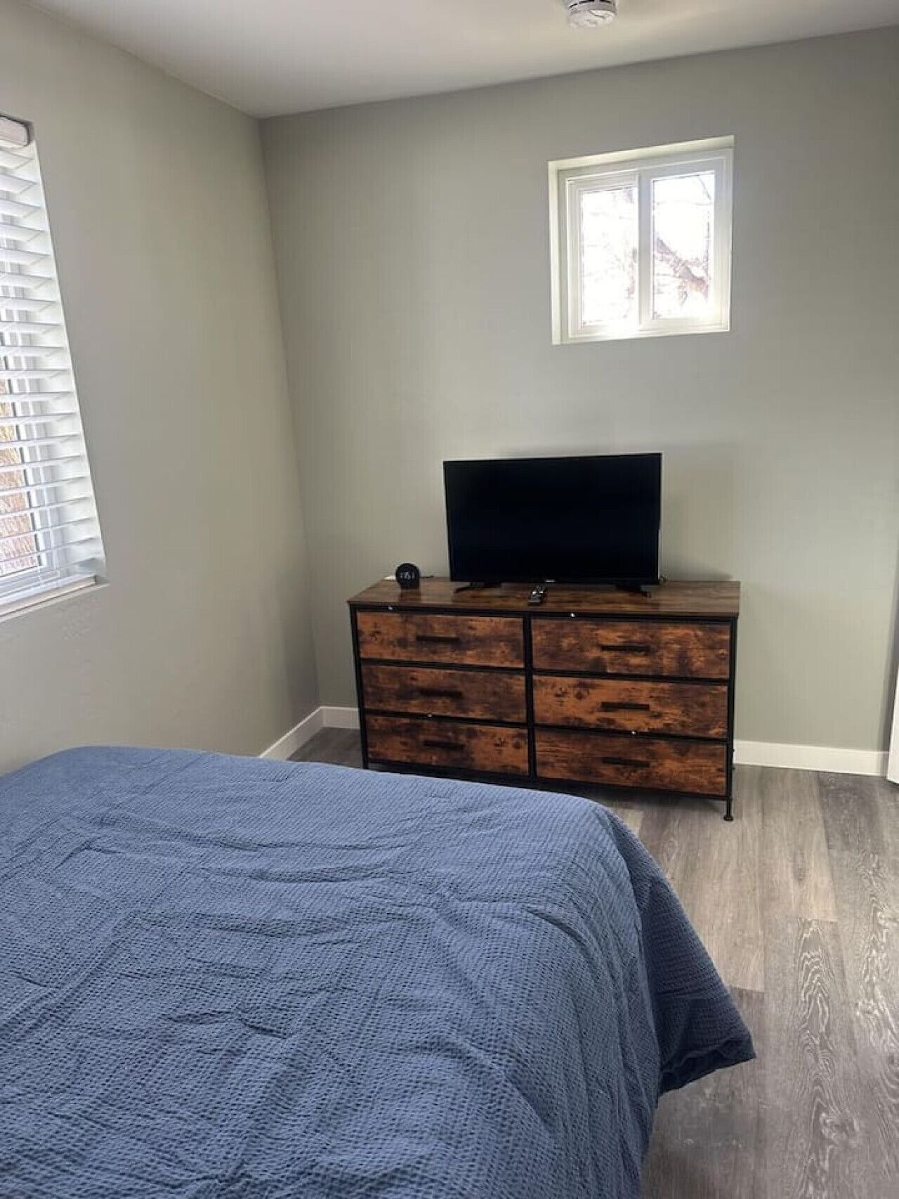A bedroom with a bed, a dresser, a television, and a window.