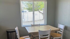 A dining area with a table and four chairs, a trash can, and a window with blinds. - *Clean *Modern Respite *WIFI *Private Yard (Prescott)