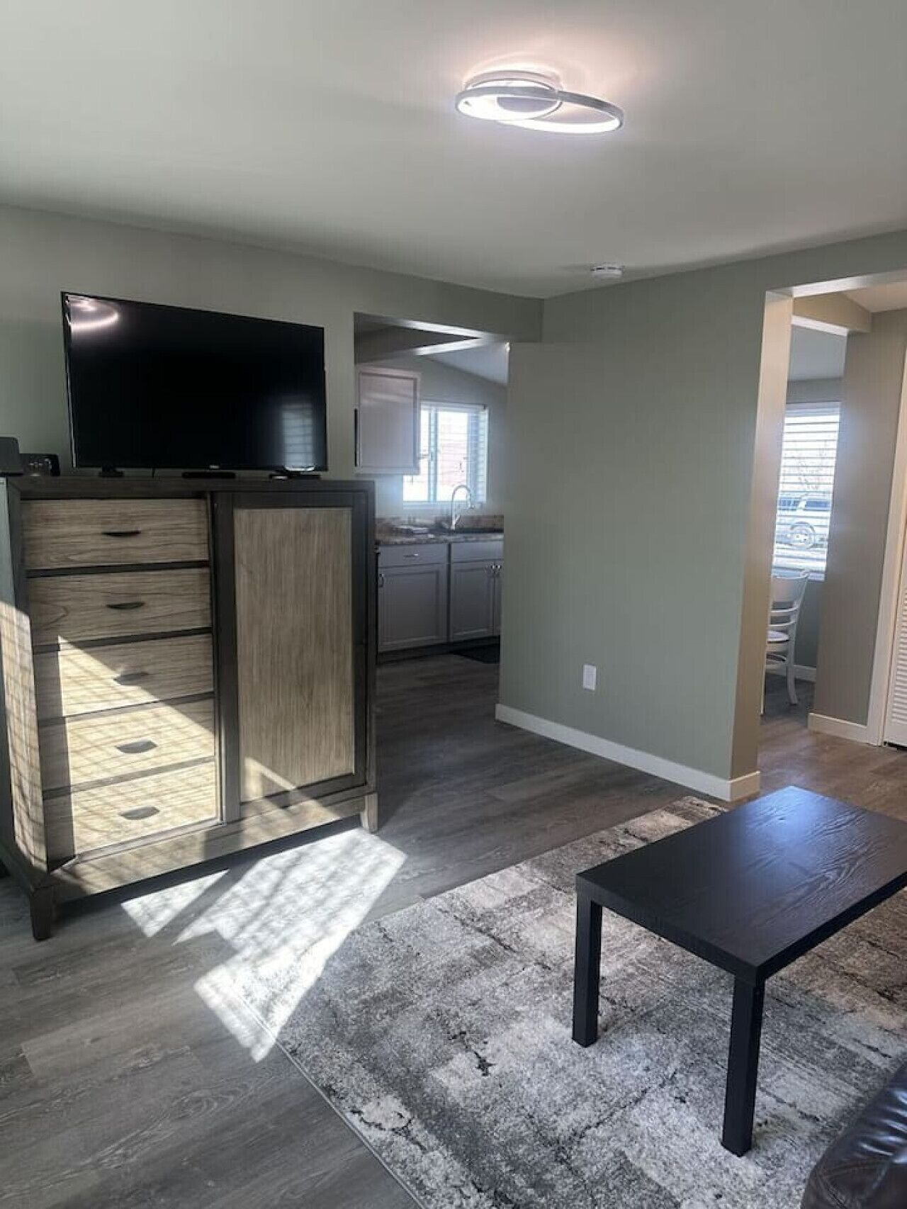 A modern living room with a flat-screen TV, wooden cabinet, and a black coffee table.