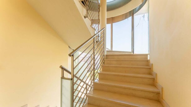 A spiral staircase with metal railings and beige steps, leading to a higher floor.