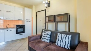 A modern kitchen with white cabinets, a black oven, and a brown sofa with patterned cushions.