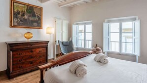 Ein Schlafzimmer mit einem Holzbett, einem Schminktisch, einem Sessel und einem Gemälde an der Wand.