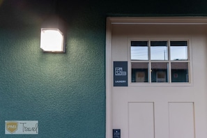 Une façade d’immeuble avec un mur végétal, une porte blanche dotée d’une fenêtre et une enseigne indiquant la présence d’une laverie.