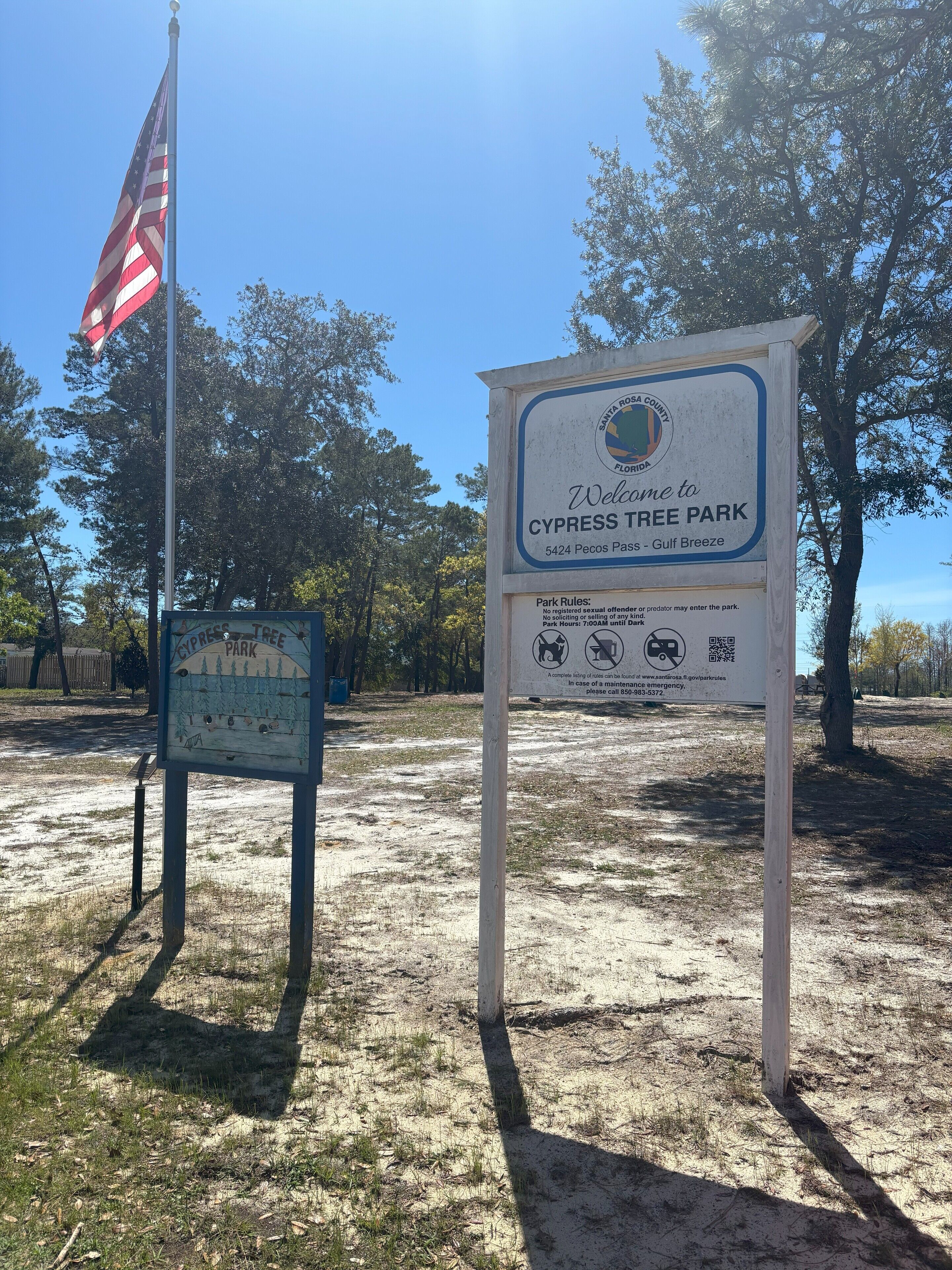 Señal de bienvenida del Parque Cypress Tree en Florida, con un asta de bandera y árboles al fondo.