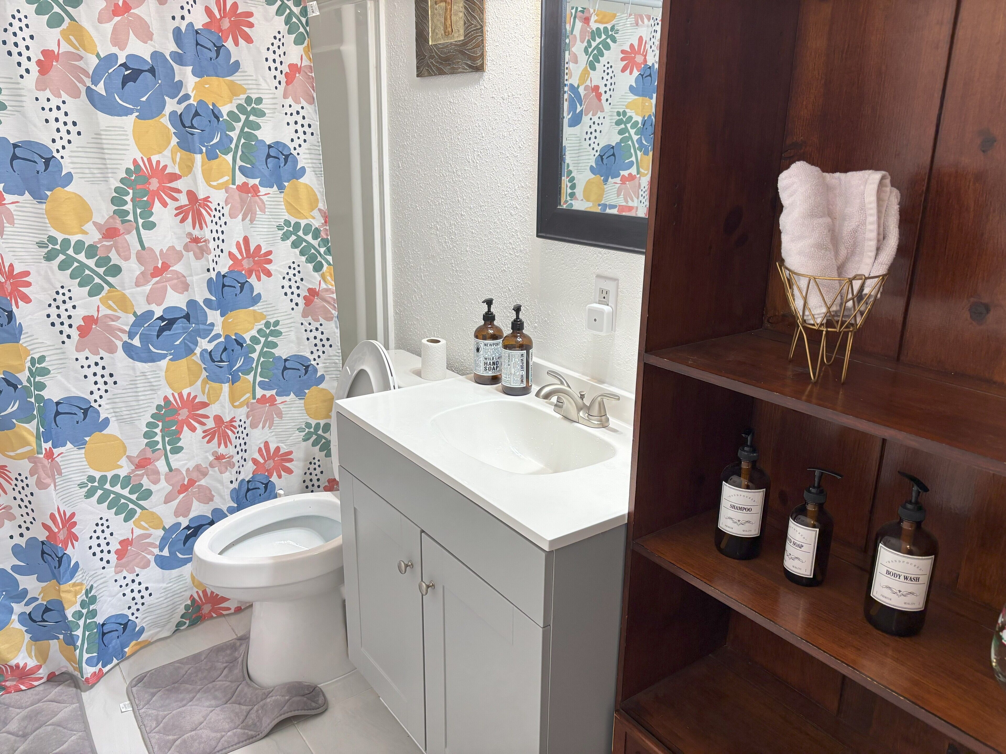 A bathroom with a white sink, a toilet, and a shower area. There are toiletries on the sink and shelves.