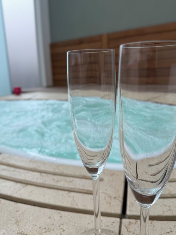 Two clear glasses on a stone surface with a hot tub in the background. - HrD Luxury rooms (Palermo)