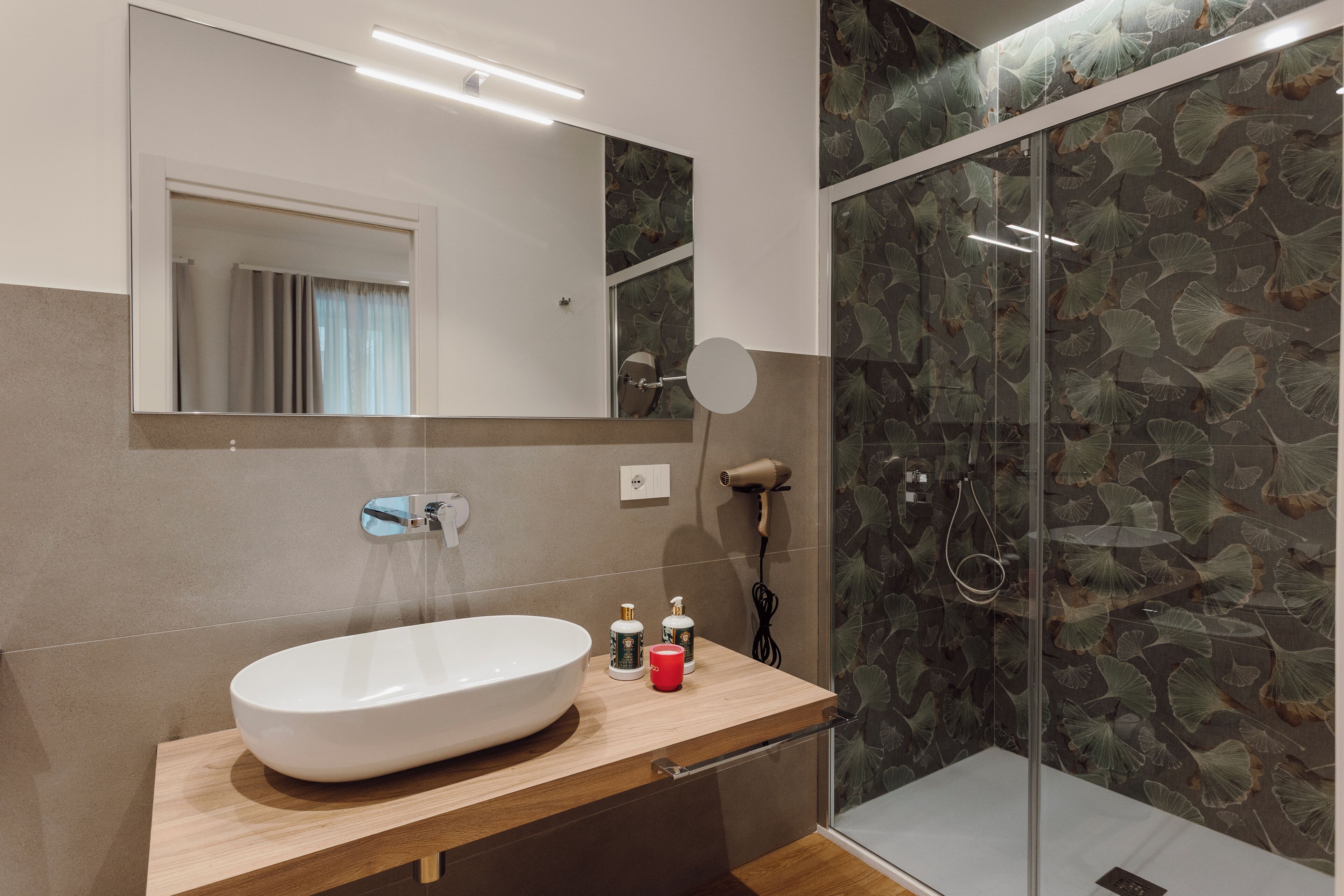 Un baño moderno con un lavamanos ovalado grande, un espejo, un cabezal de ducha manual y una ducha con mampara de vidrio.
