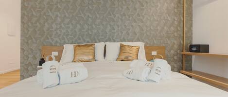 A hotel room with a bed, two pillows, a wooden headboard, a bedside table with a black object, and a wall with a honeycomb pattern.