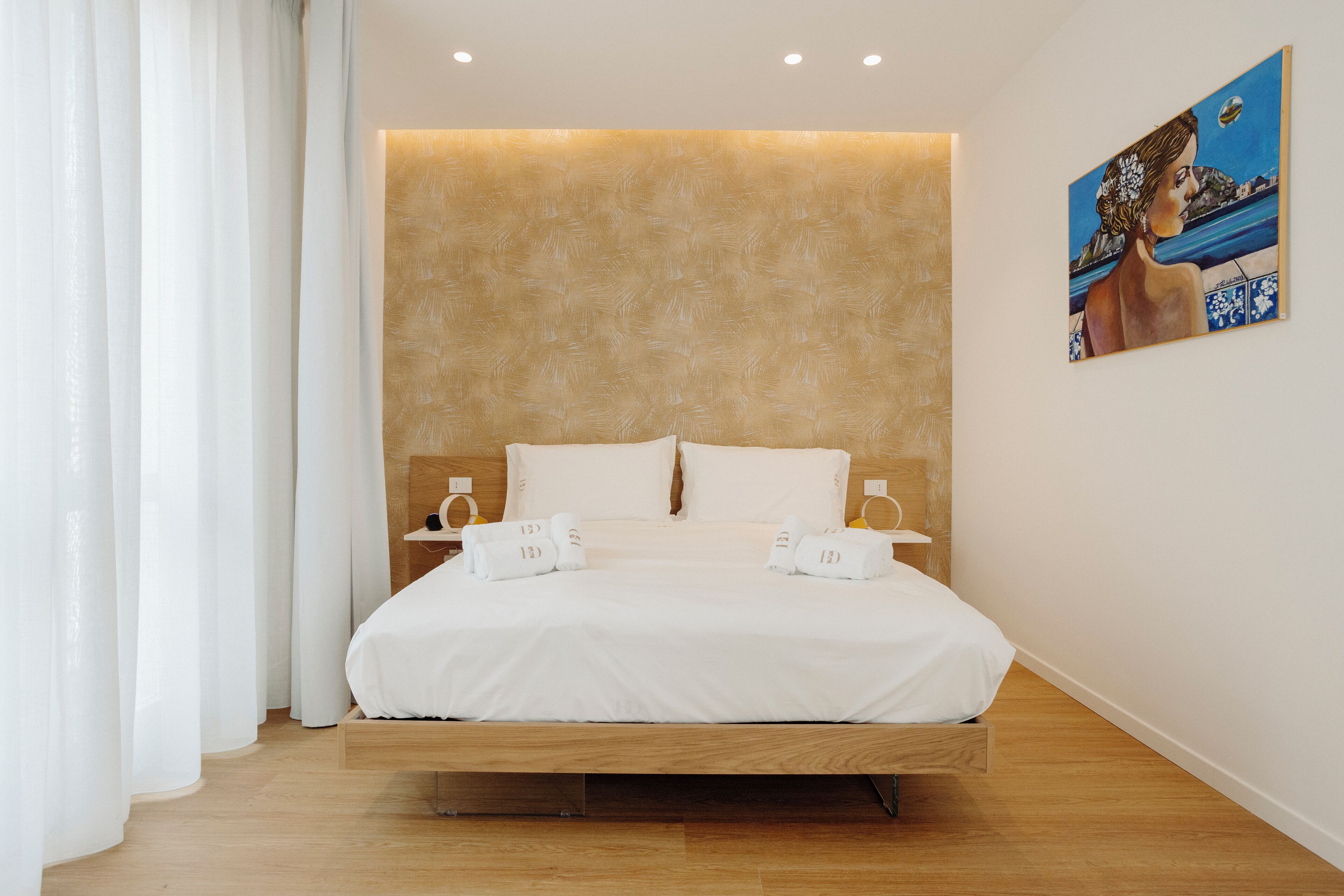 Una habitació d'hotel moderna amb un llit de fusta, roba de llit blanca i un quadre a la paret.