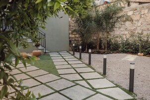 Un sendero pavimentado con bordes de césped que lleva a un edificio con pared de piedra y una escalera.