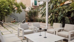 Un'area patio con arredi bianchi, tra cui divani e un tavolo, immersa nel verde e con una scala.