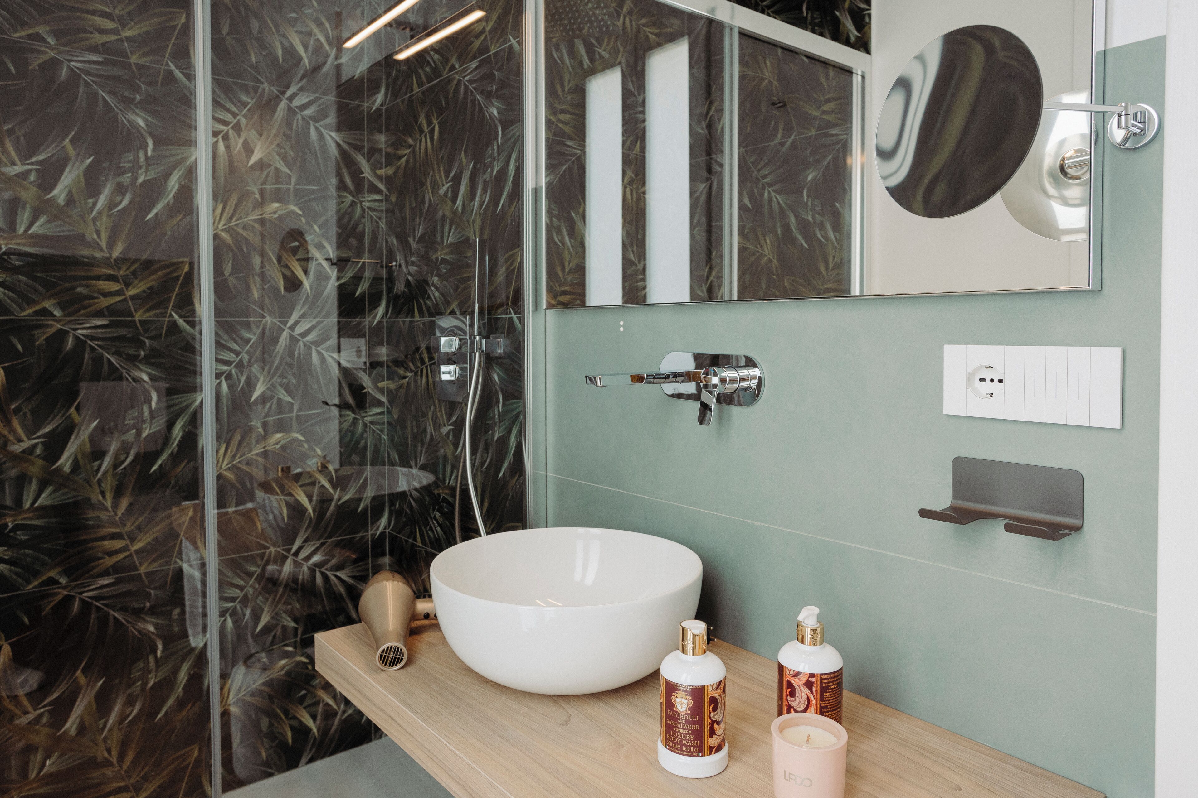 Une salle de bain avec un grand lavabo blanc, un miroir et une douche dotée d’une porte en verre. On trouve des articles de toilette sur le comptoir.