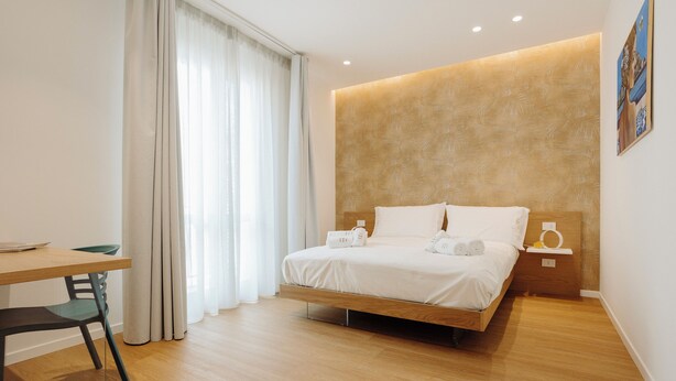Una camera d'albergo moderna con un letto di legno, un comodino, una scrivania e una sedia.
