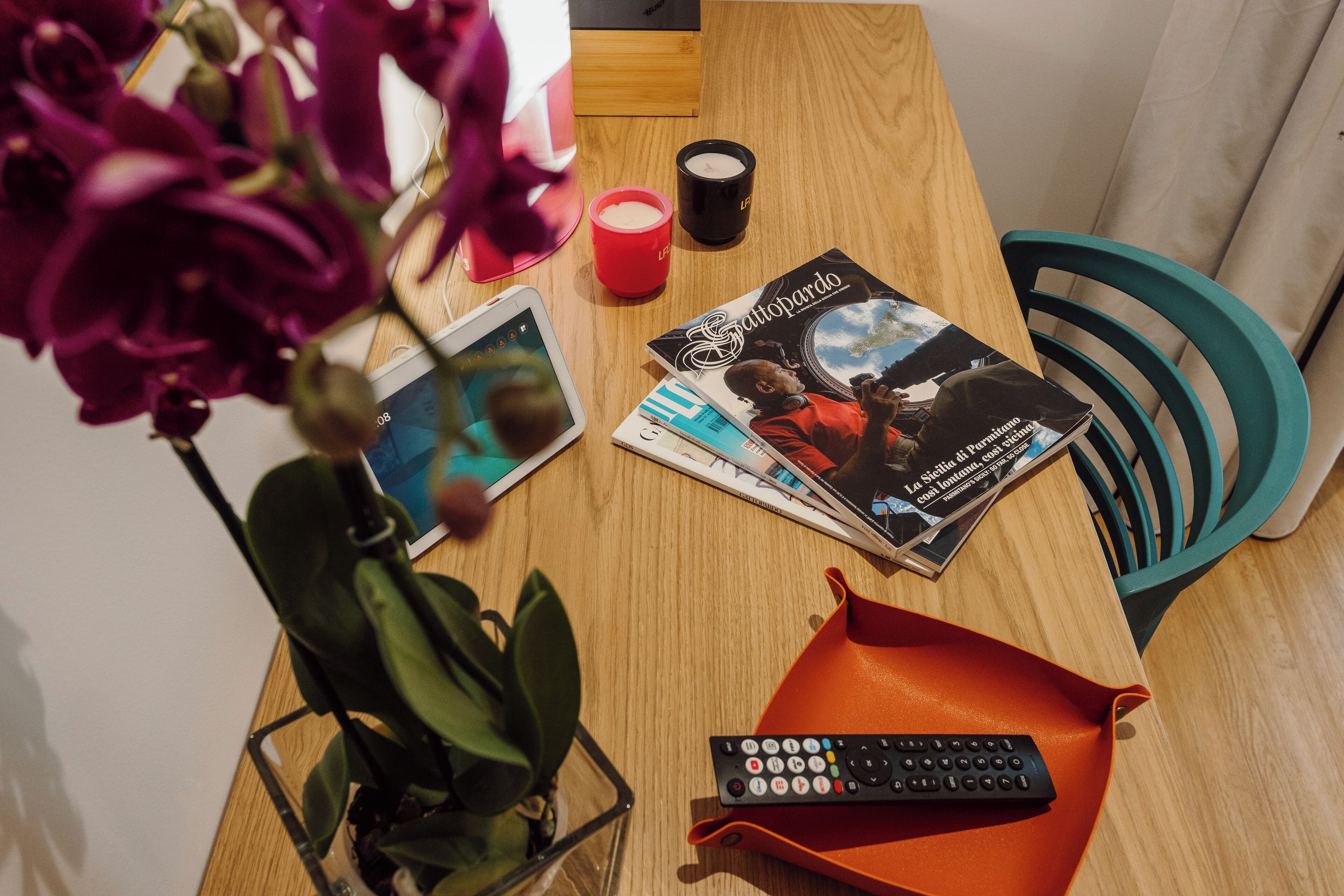 Une table en bois avec une télécommande, un magazine, une bougie rouge et une plante en pot.