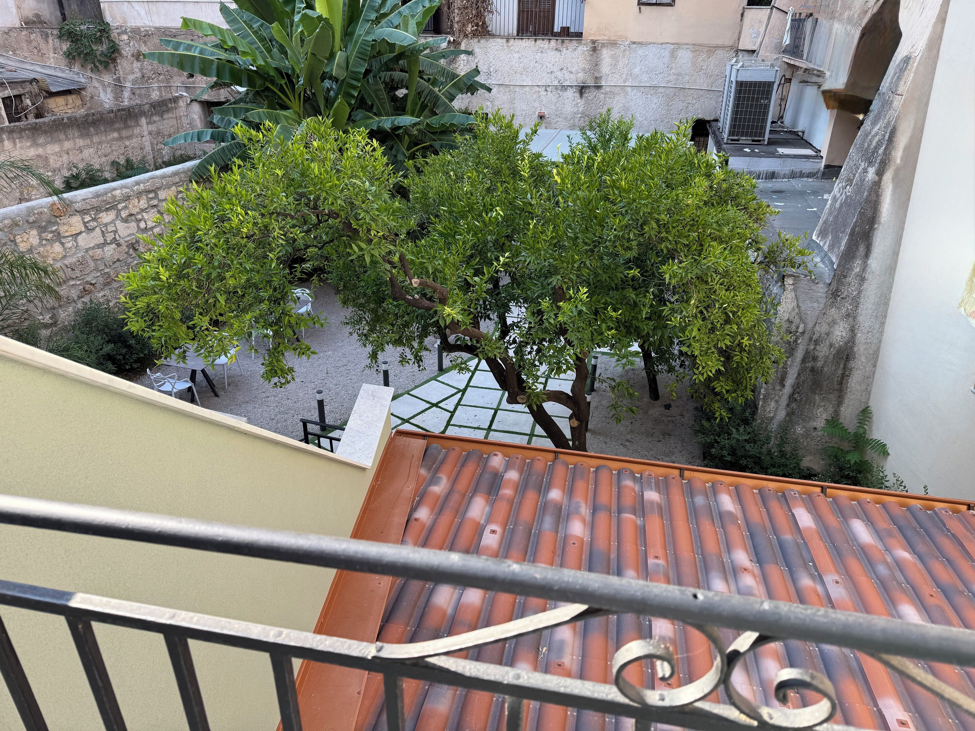 A courtyard with a tiled roof, a tree, and a stone wall.