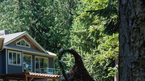 Una casa en árbol de diseño circular, una vivienda al fondo y una zona cubierta de césped.