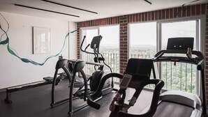 Et fitnesscenter med træningsudstyr, store vinduer og udsigt over byen.