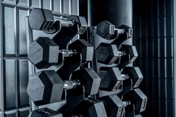 Un juego de mancuernas hexagonales negras dispuestas en un soporte frente a una pared metálica.