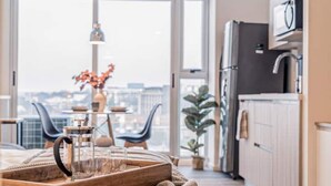 Une cuisine moderne avec un plan de travail en bois, une machine à café et une vue sur la ville grâce à de grandes fenêtres.