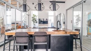 Une cuisine moderne dotée d’un grand îlot central, de tabourets de bar, de luminaires suspendus et offrant une vue sur la ville grâce à de grandes fenêtres.