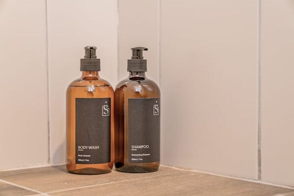 Two bottles of body wash and shampoo on a tiled floor against a white wall.