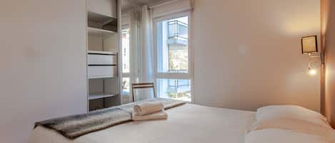 Une chambre à coucher comprenant un lit, une armoire, une fenêtre et un luminaire fixé au mur.