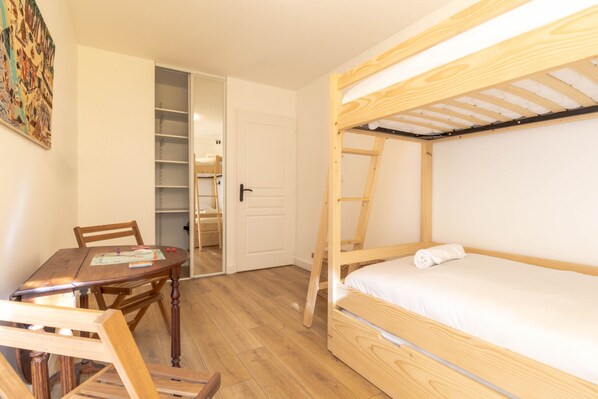 Une chambre avec un lit superposé, une table et des chaises en bois, une bibliothèque et une porte donnant sur un placard.