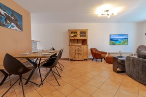 Un coin repas avec une table en bois dressée pour quatre personnes, entourée de chaises modernes, d’un meuble avec des portes en verre et d’un téléviseur diffusant un paysage pittoresque.