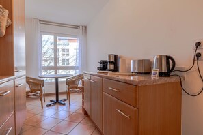 Une cuisine compacte avec un coin repas, comprenant une machine à café, une bouilloire et une petite table avec des chaises.