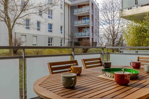 Une table en bois, entourée de chaises, sur un balcon délimité par une balustrade.