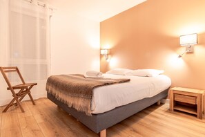 Ein Schlafzimmer mit einem Bett, Holzboden, einem Sessel, einem Nachttisch und Wandleuchten.