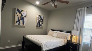 A bedroom with a bed, a nightstand, a ceiling fan, and two abstract paintings on the wall. - Charming 1-bedroom apartment with WiFi, AC in gorgeous Sour Lake #211 (Sour Lake)
