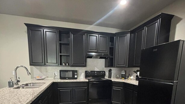 A modern kitchen with dark cabinetry, a stainless steel sink, a microwave, a stove, and a black refrigerator. - Charming 1-bedroom apartment with WiFi, AC in gorgeous Sour Lake #211 (Sour Lake)