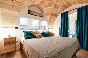 A bedroom with a stone ceiling, a bed with a patterned bedspread, and a view of the sea through a window. - Prince 25 - Lecce Selection (Lecce)