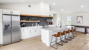 A modern kitchen with white cabinets, a stainless steel refrigerator, a central island with bar stools, and a black backsplash. - Bungalow on 3 Acres - Hot Tub& Firepit (McKinney)