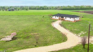 A rural property with a single house, a gravel driveway, and expansive green fields. - Bungalow on 3 Acres - Hot Tub& Firepit (McKinney)