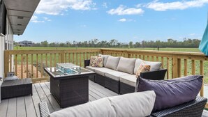A covered outdoor deck with wicker furniture, a glass-top table, and a view of a green field. - Bungalow on 3 Acres - Hot Tub& Firepit (McKinney)